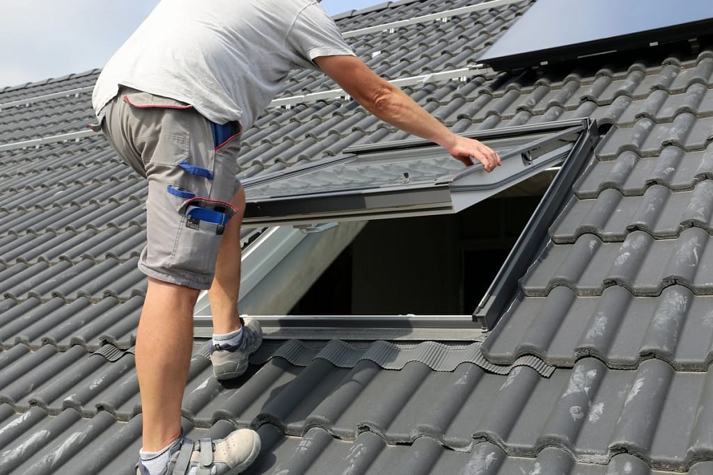 Worker installing a skylight within a black tile roof
