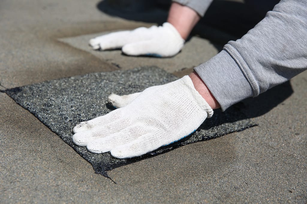 a patch of bitumen sheet for roof. local repair of roof waterproofing. hands of worker are tamping the patch on the roof