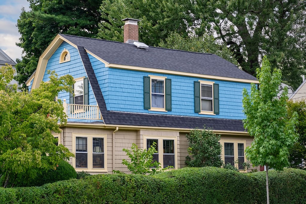 Blue house with gambrel roof in distance behind greenery