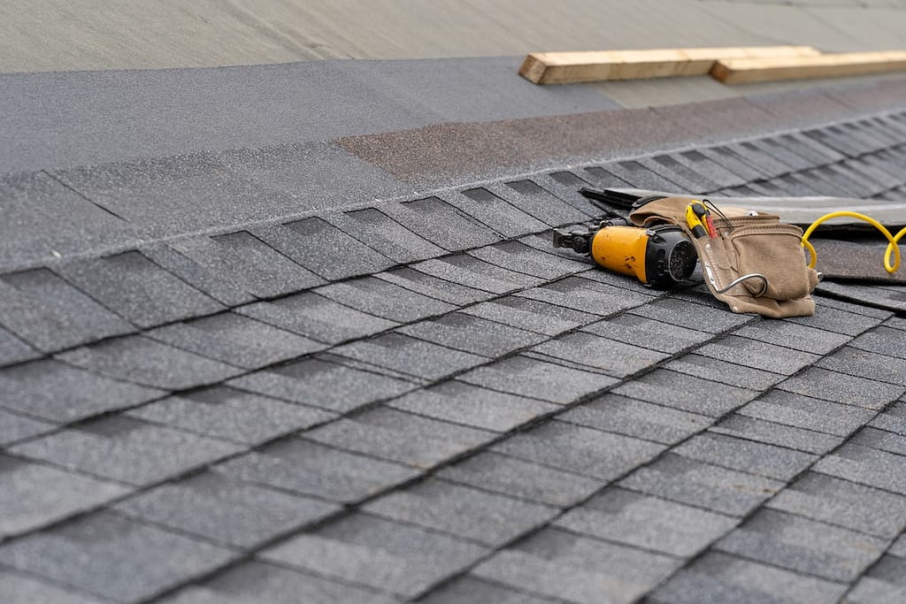 Photo of toolbelt with instrument and nail gun lying on asphalt shingles
