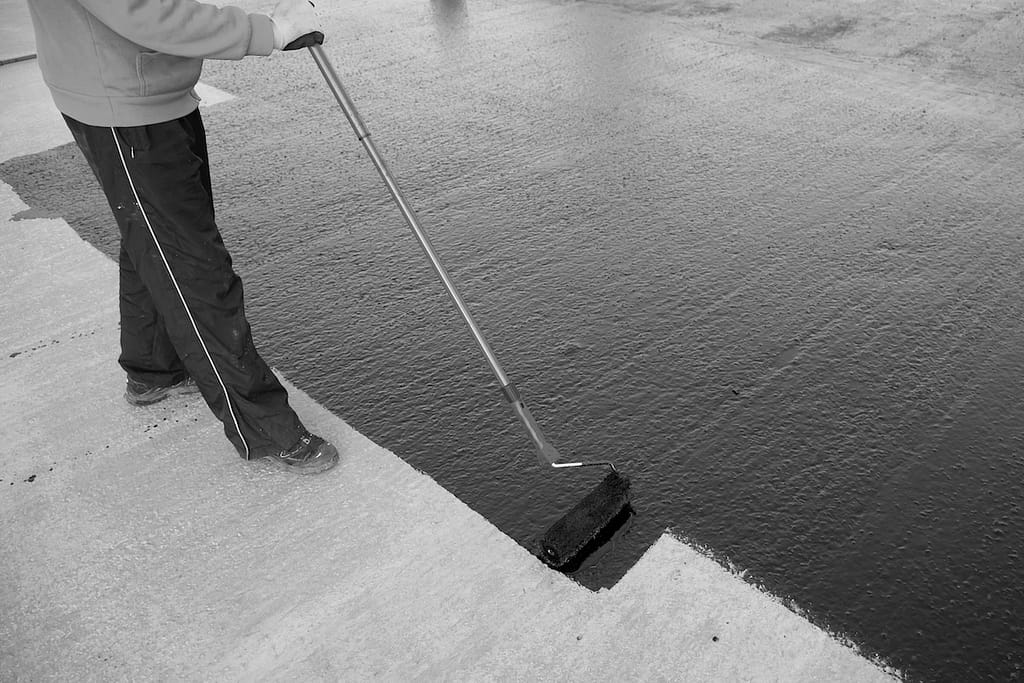 Waterproofing coating. Worker applies bitumen  with a roller brush.