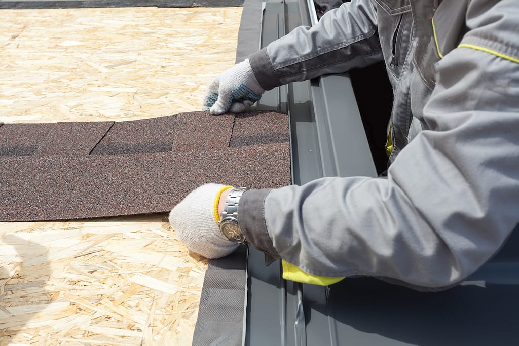 professional roofer worker lays asphalt sheet on the rooftop, holding roof tile in hands