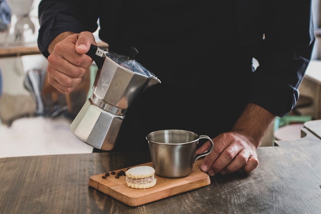Male Barista preparing fresh espresso in coffee maker for customer in a coffee shop.