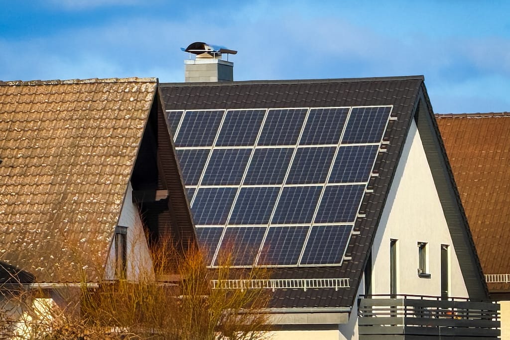 A modern house features solar panels on its roof, showcasing sustainable energy use under a bright blue sky in the daytime.