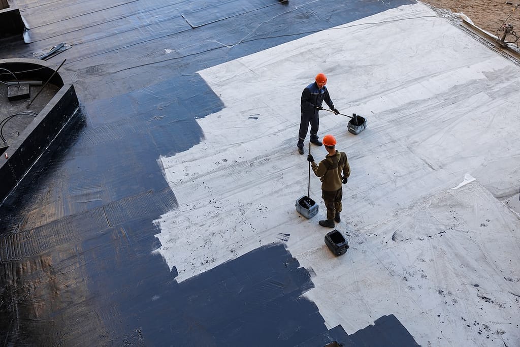 Waterproofing coating. A worker applies bitumen mastic to the foundation. Roofer cover the waterproofing primer on the roof, modified with polymer bitumen, with a roller brush.
