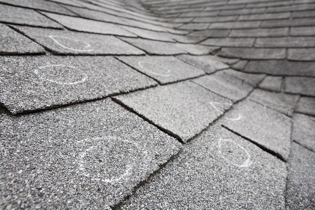 Old roof with hail damaged shingles, chalk circles mark the damage