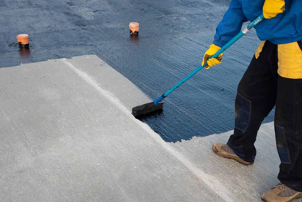 Waterproofing coating. Worker applies bitumen mastic on the foundation. Roofer cover the rooftop polymer modified bitumen waterproofing primer, with a roller brush.
