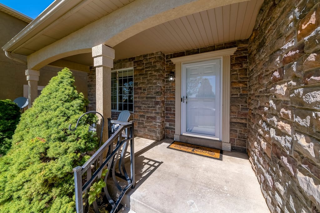 White front door with glass storm door and decorative how to install a storm door doorframe. There is a railings on the left near the topiary shrub and a wall on the right with stone veneer. how to install a storm door