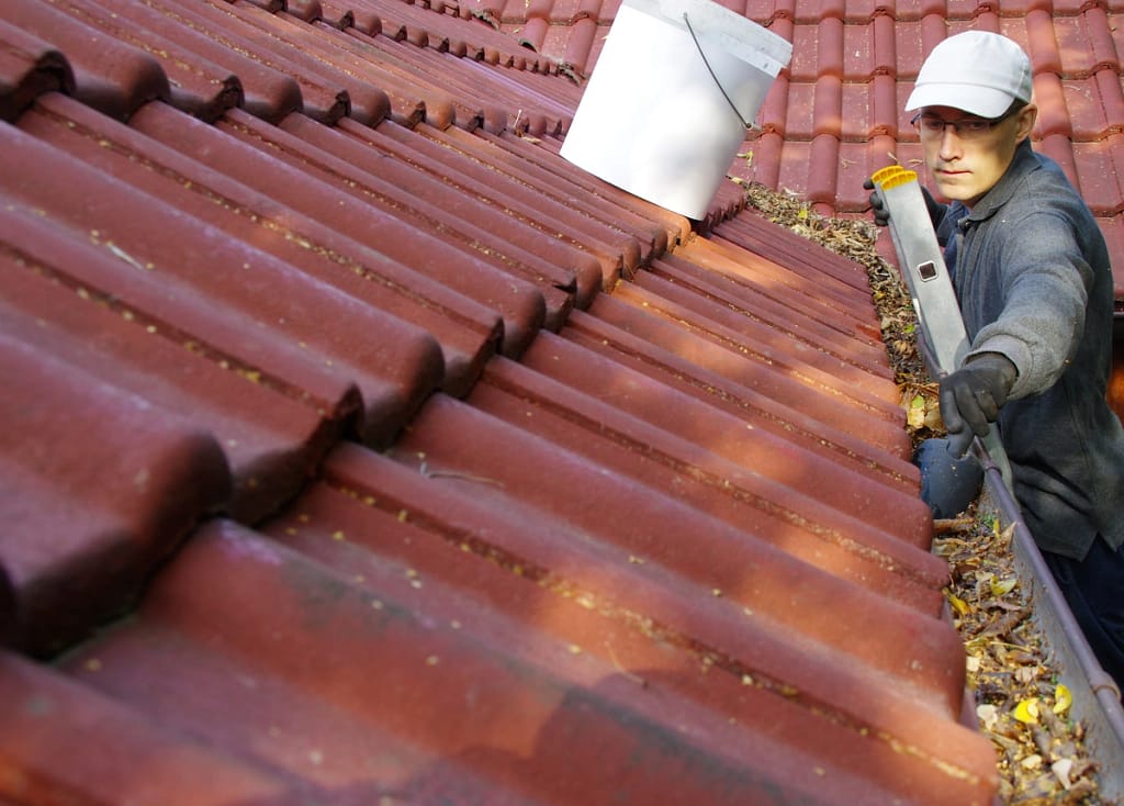 homeowner cleans gutters during DIY roof maintenance