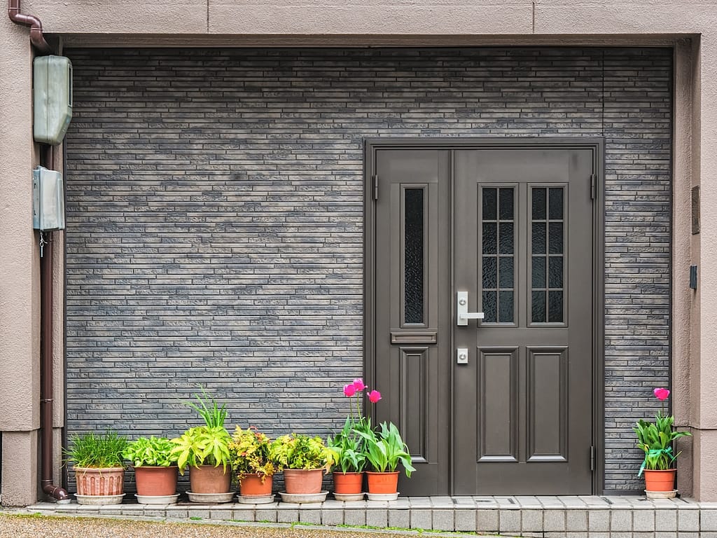 Gray front door with small square decorative windows and tiled concrete wall with flower pots in front of it front door colors