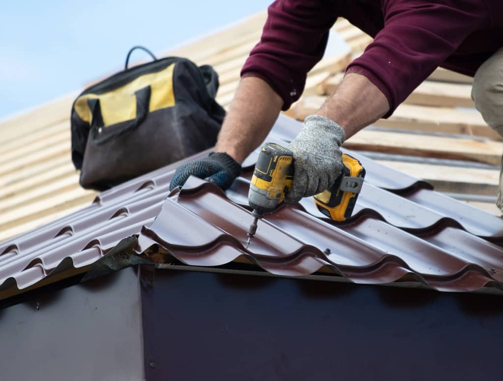 worker using drill to install metal tiles on roof