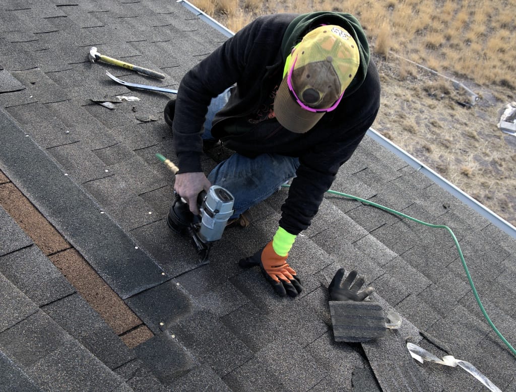 worker using nail gun to place asphalt shingles on roof