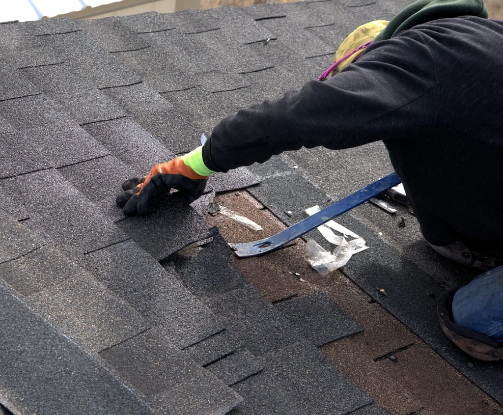 roofer using a pry bar to remove shingles