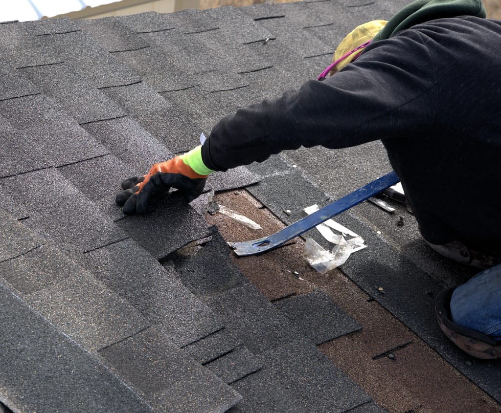 close up of diy roof replacement removing shingles with pry bar