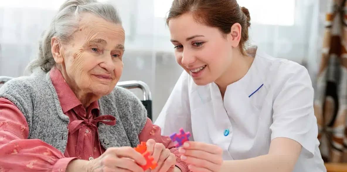 An elderly woman works on a puzzle with a nurse