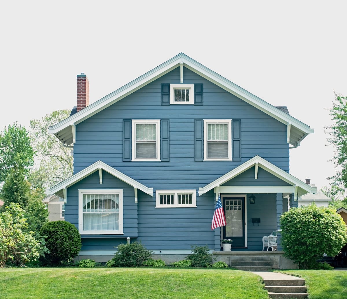 A two-story blue house with white trim features a gabled roof and several windows