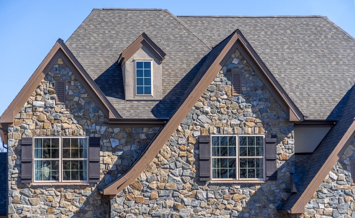 Double gable with dark stone veneer siding, with triangle shape peaks, on a pitched roof attic at an American single family home neighborhood USA, double sash windows w/ matching dark shutters