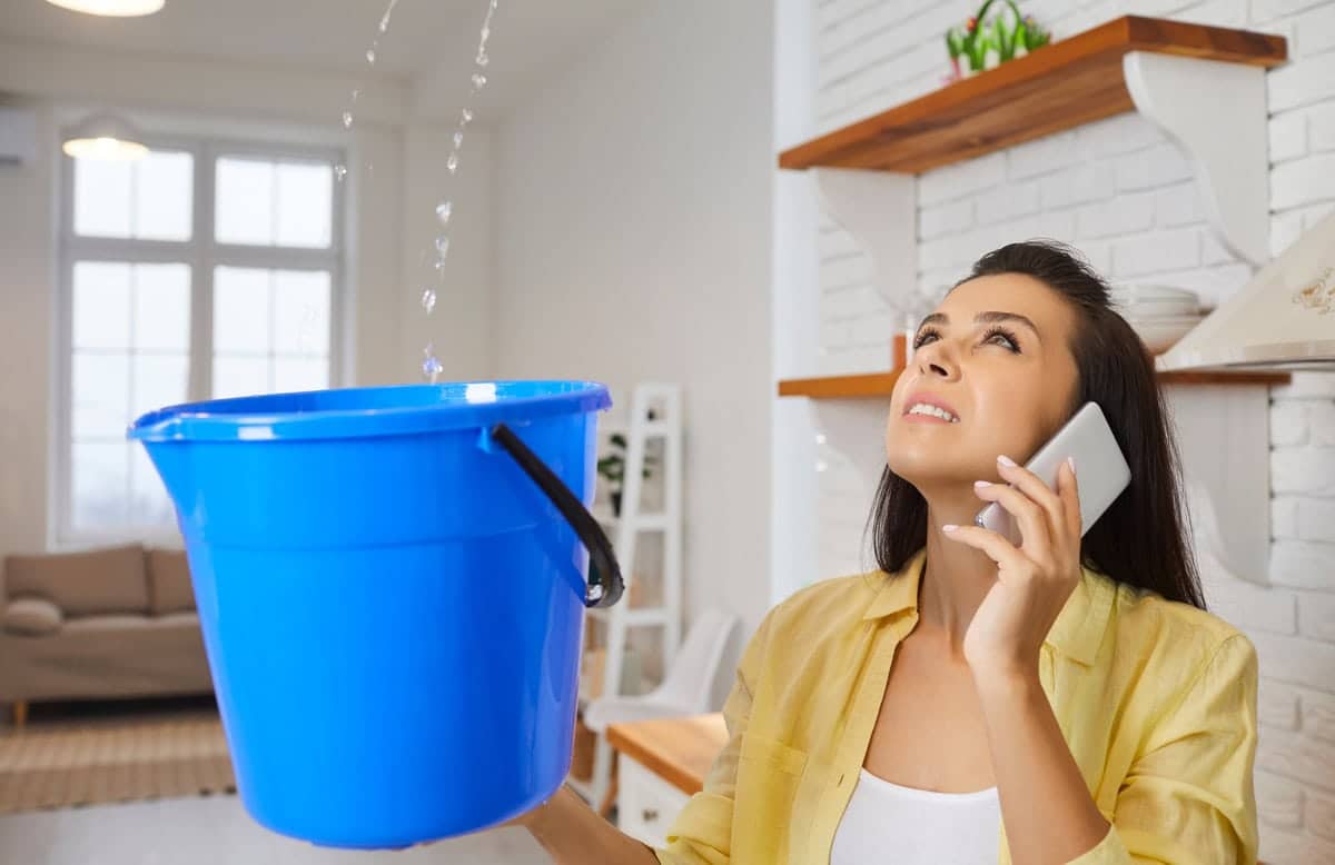 a woman is collecting leakage water from ceiling with help of a bucket