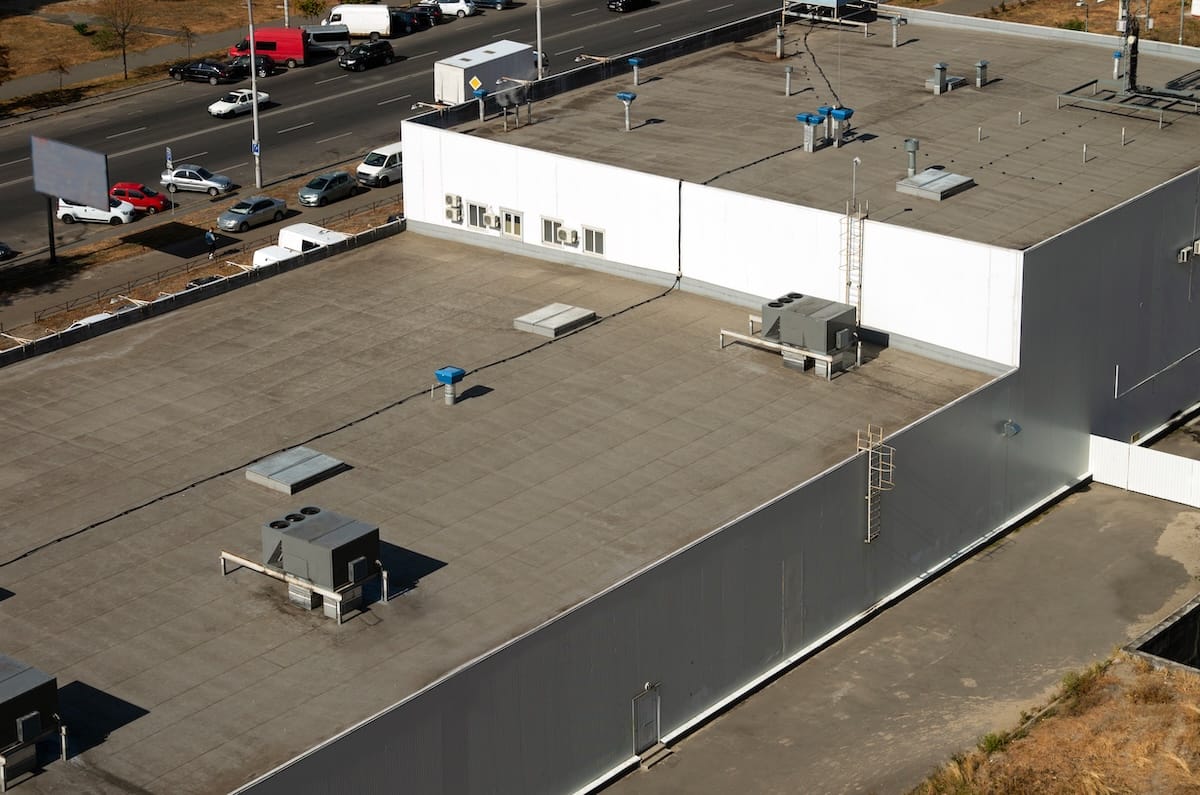 A large flat rooftop with energy efficient roofing, multiple air conditioning units, ventilation systems, and a metal ladder