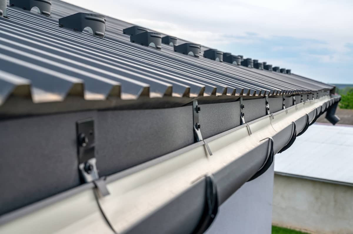 Close-up view of a modern metal roof with a gutter system, featuring neatly installed black roofing sheets and drainage components