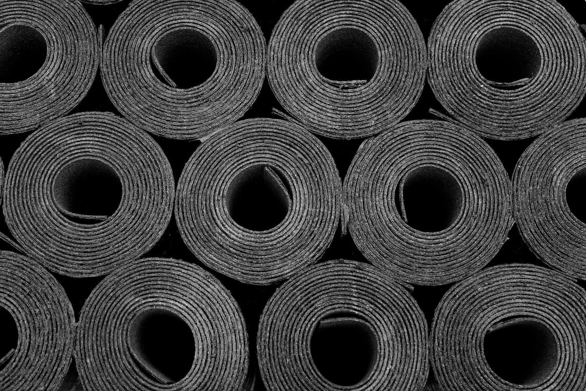 Close-up view of multiple tightly rolled roofing material, arranged in a neat grid pattern, with the circular ends facing the camera and forming repetitive concentric circles.