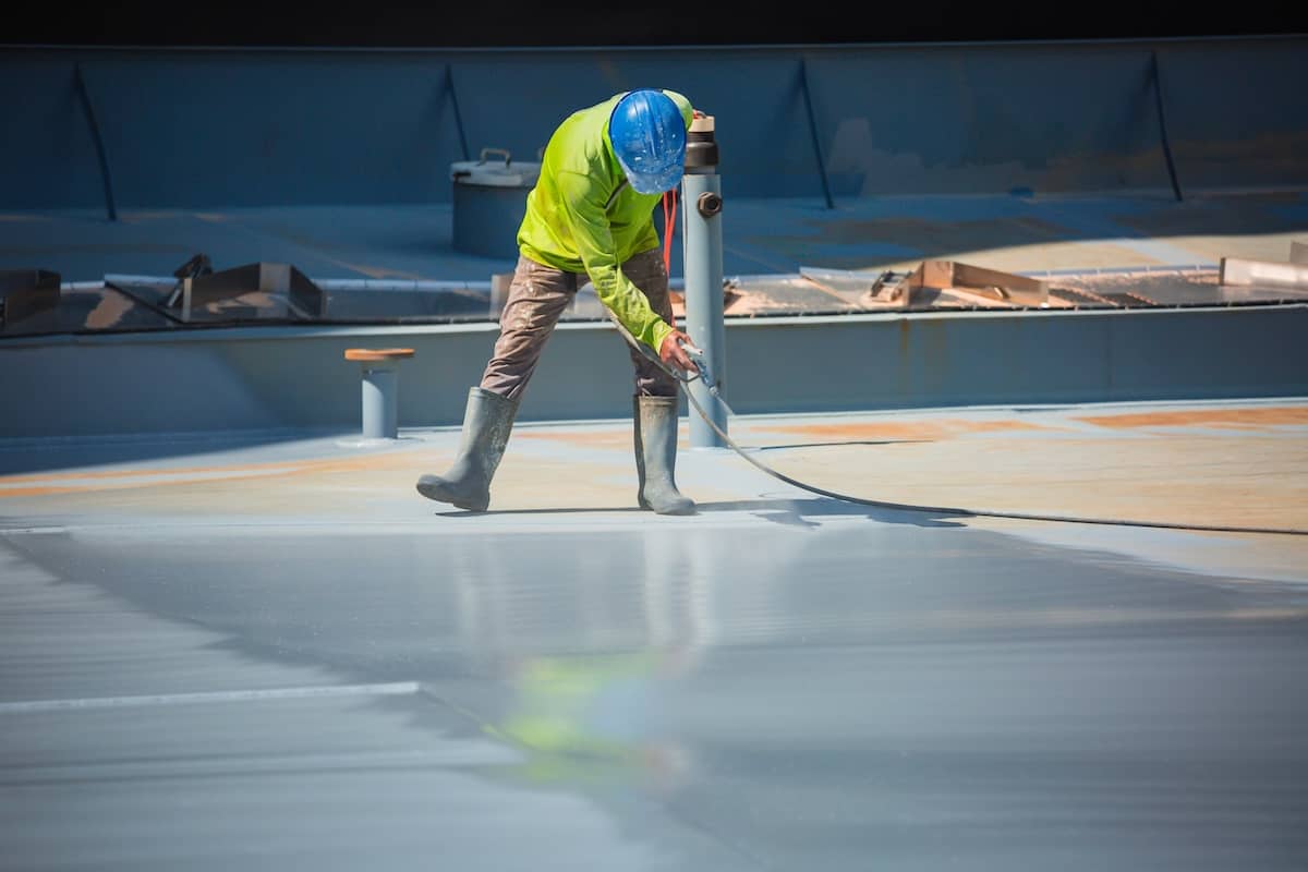 Worker in a bright green jacket sprays a coating on a industrial roof