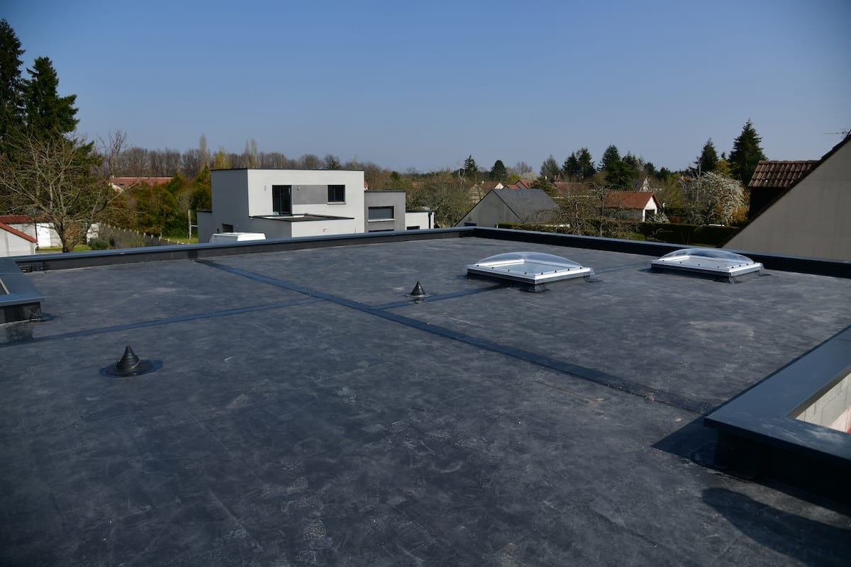 Flat rooftop of a modern building with a black EPDM roof membrane, two dome-shaped skylights, and small vents
