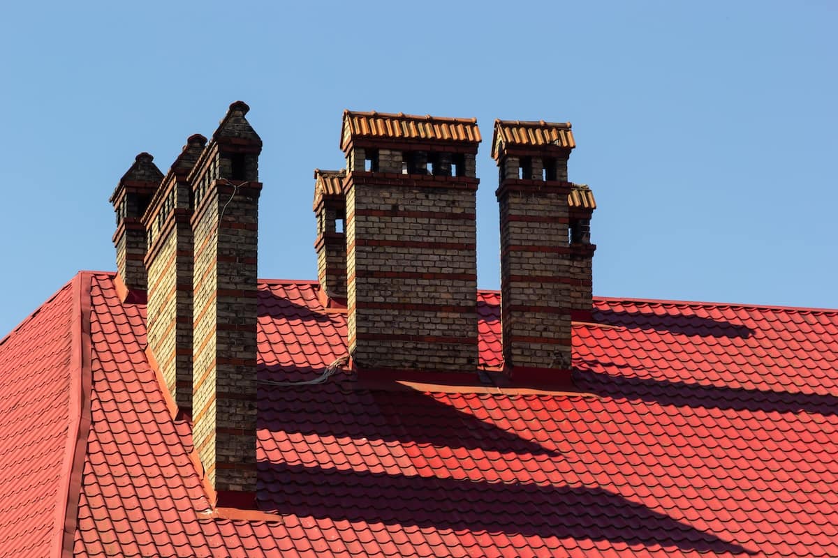 Red house roof with red brick chimney. Ceramic chimney, metal roof tiles, gutters.
