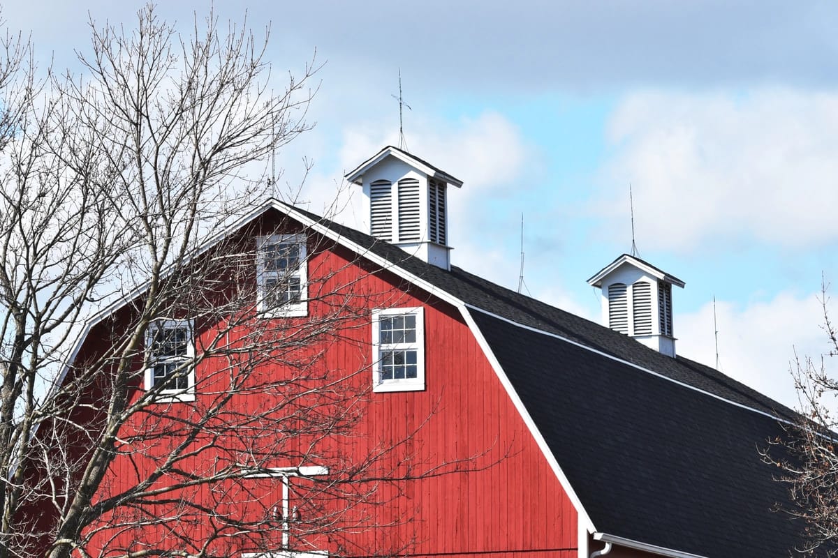 Red barn with shingle roof and two cupola roof vents.