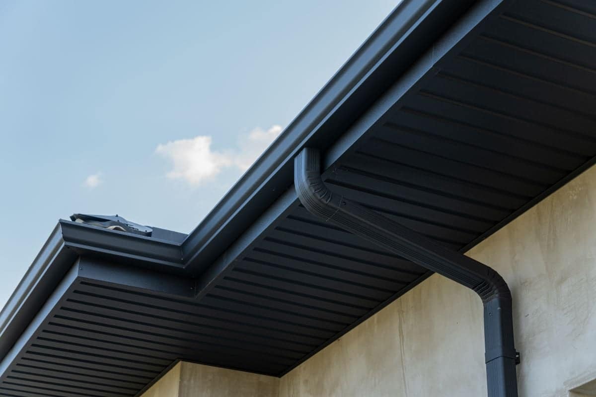 Close view of a roof edge and downspout against a bright blue sky highlights contemporary construction features and materials
