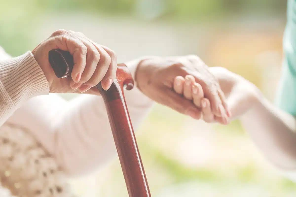 An elderly woman holds a cane with one hand and holds hands with her other