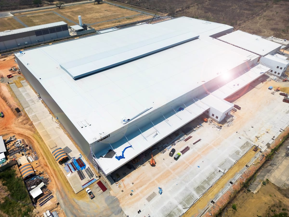 Aerial view of a large, white industrial warehouse with a flat roof to pitched roof transition
