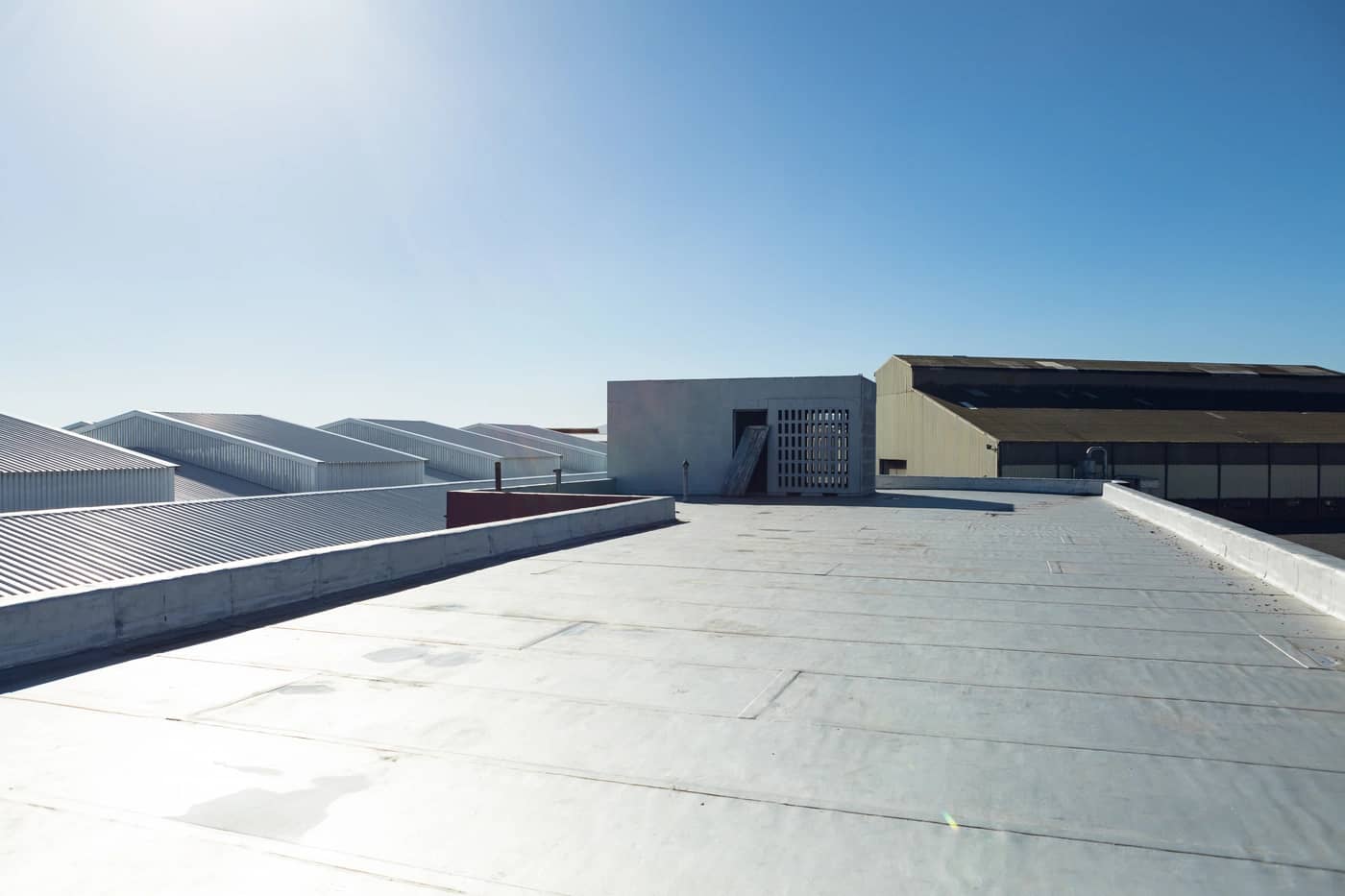 Industrial rooftop view with flat surfaces and metal structures. Several buildings with modern, angular designs are visible under a clear blue sky