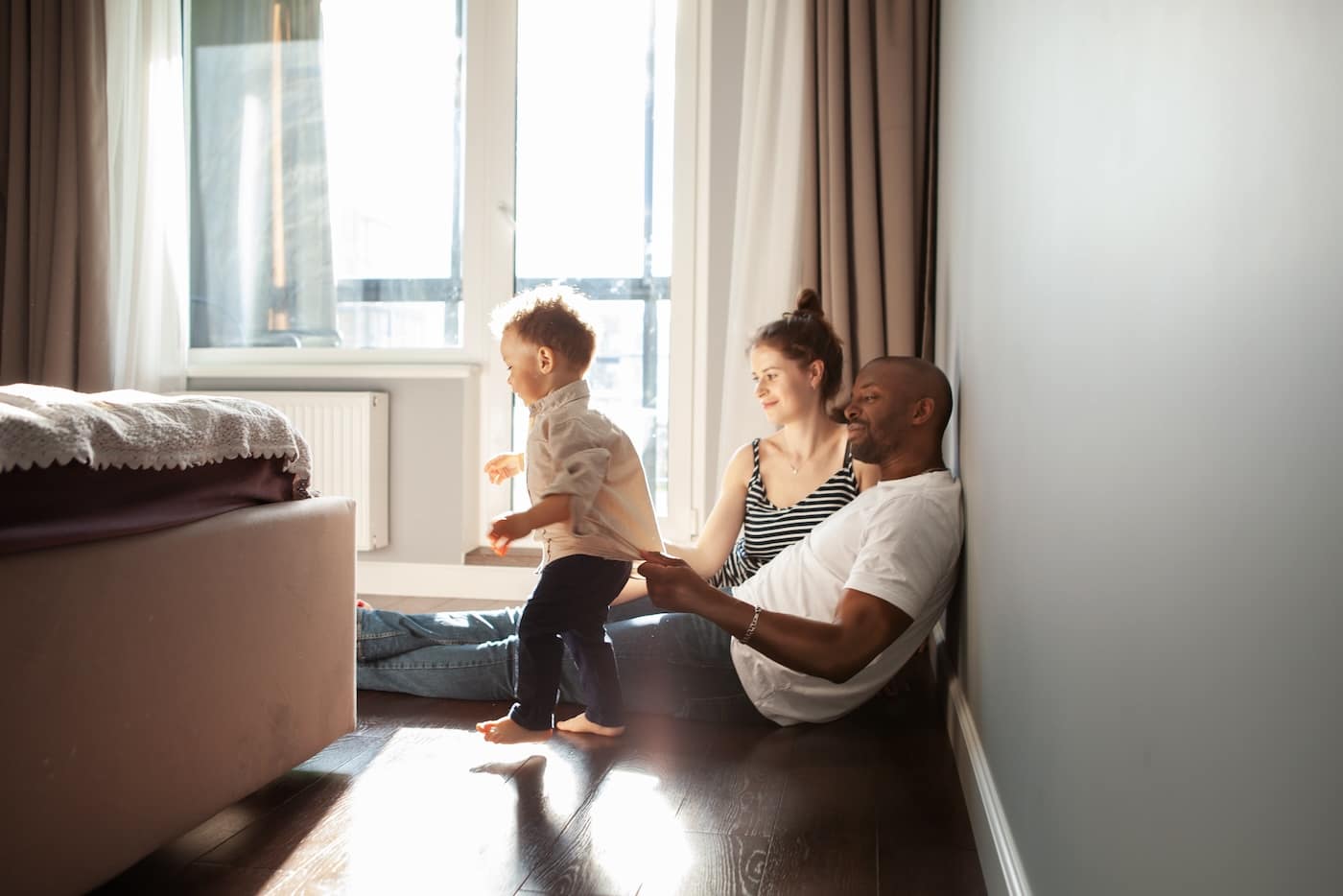 family playing with child son at home, authentic family life, unposed, spontaneous moments. Baby learning walk and dad supports him, helps.