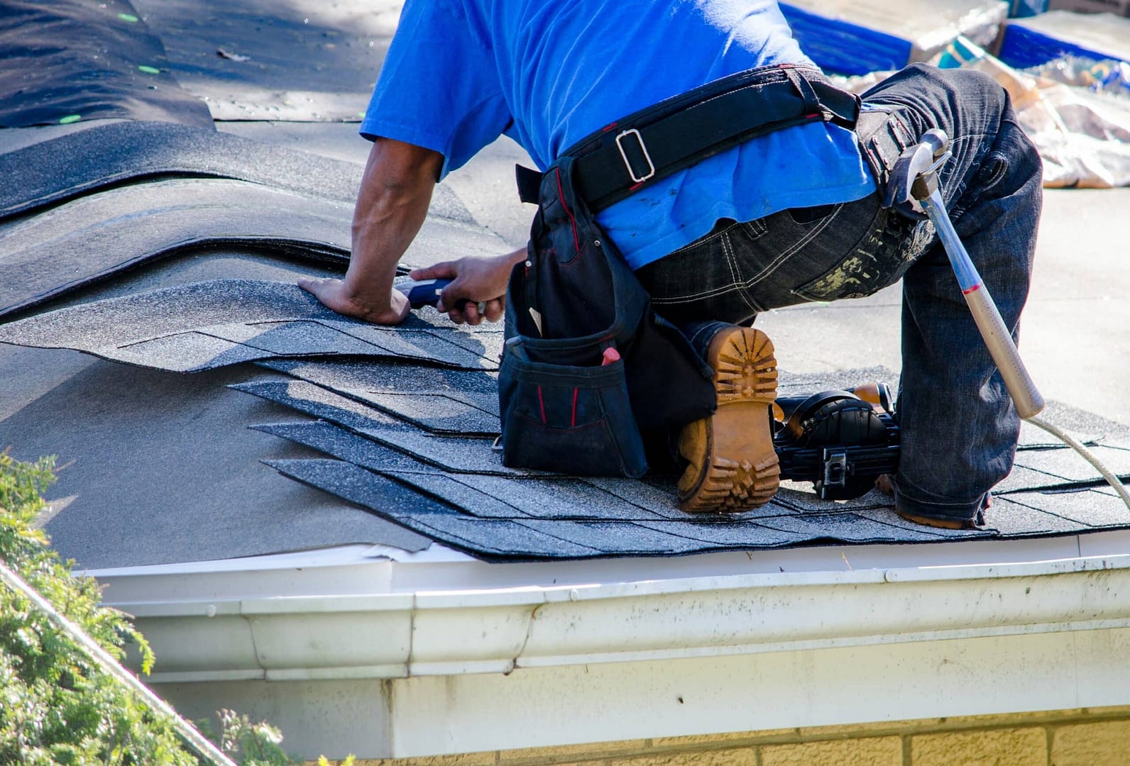 male worker on roof cutting asphalt shingles to size