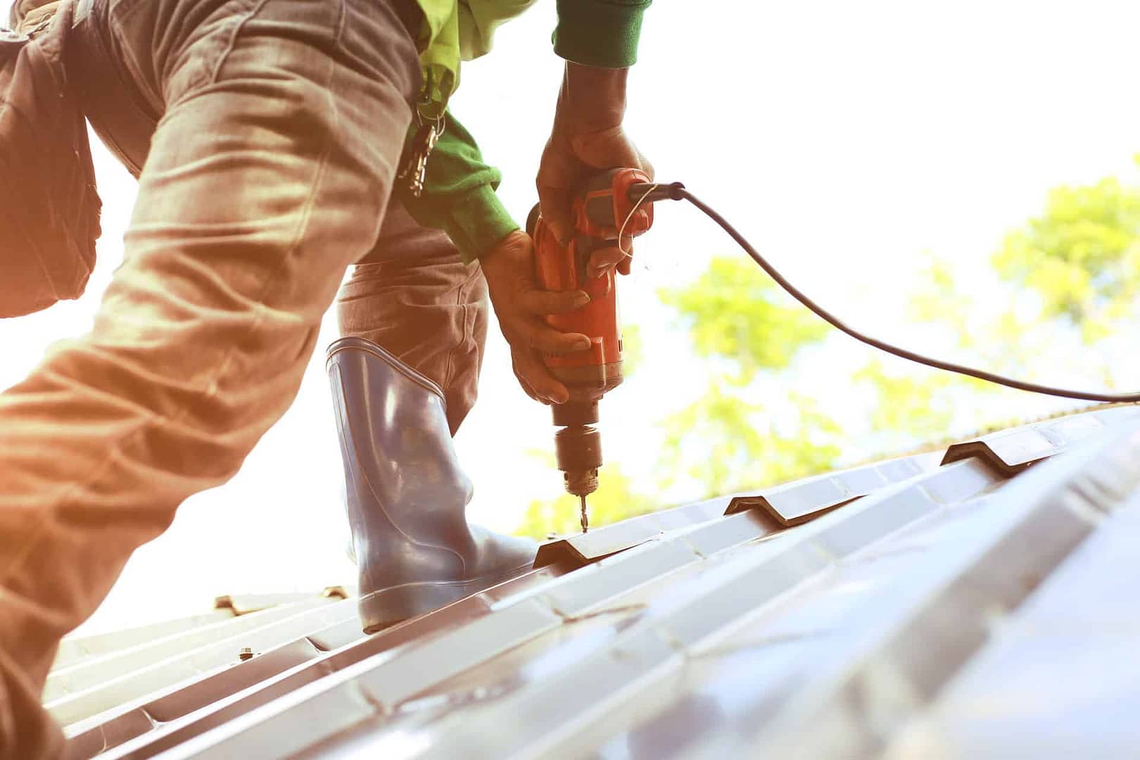 man standing on roof installing metal roofing with large nail gun
