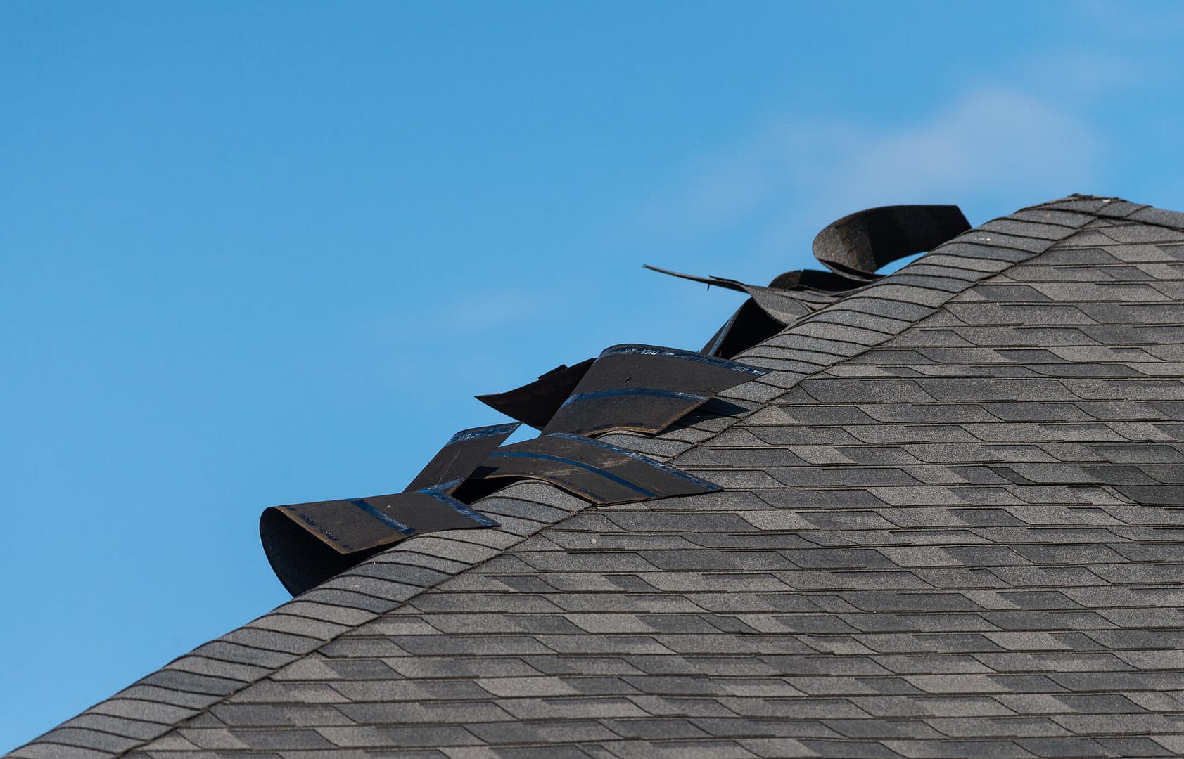 wind damage to roof-profile view of listed shingles on a gray roof