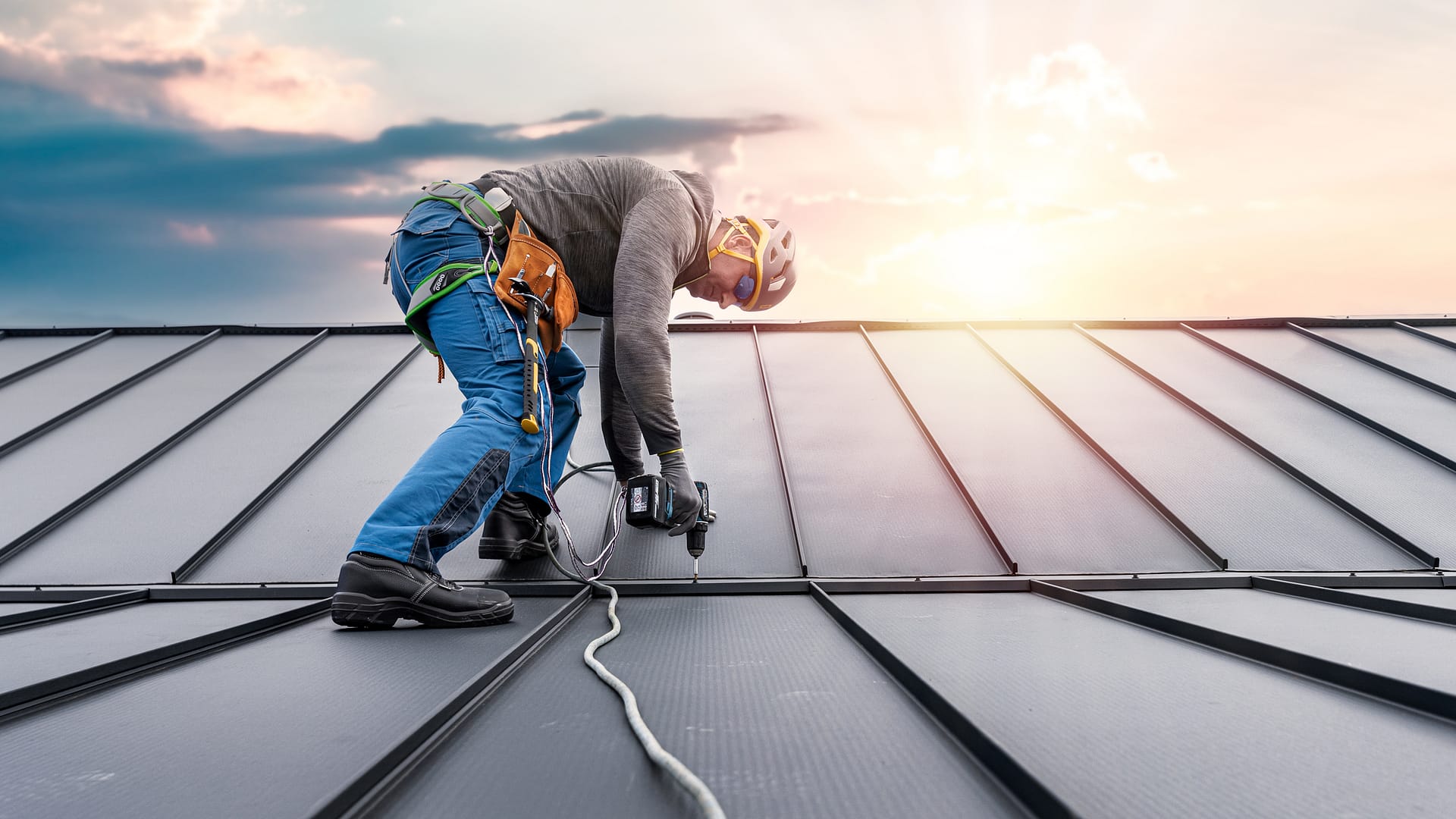 metal roof cost-roofer wearing safety gear installing standing seam metal roof on a house