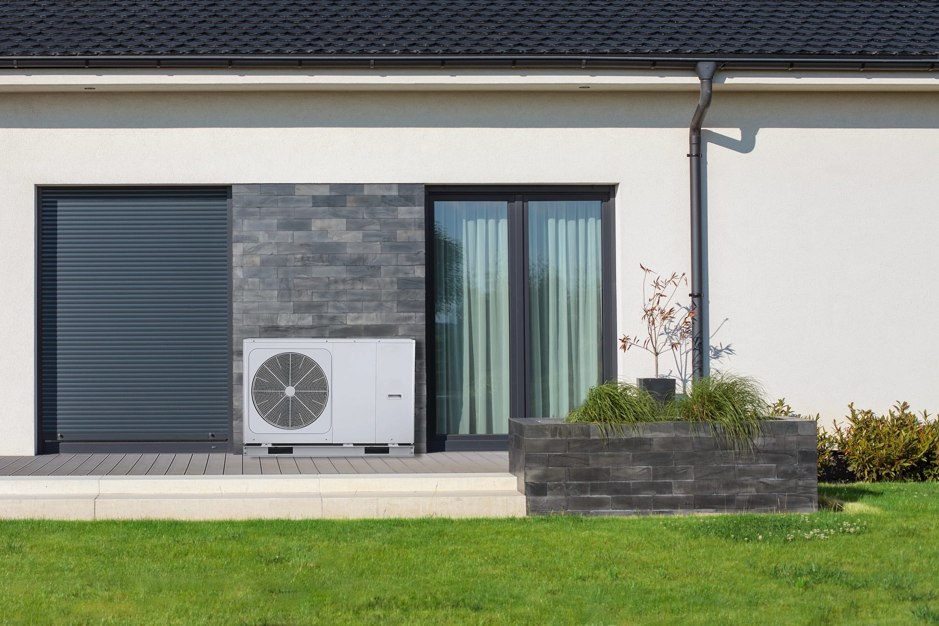 An ecological air heat pump stands beside a modern house with a lush lawn, showcasing sustainable and eco-friendly heating solutions.