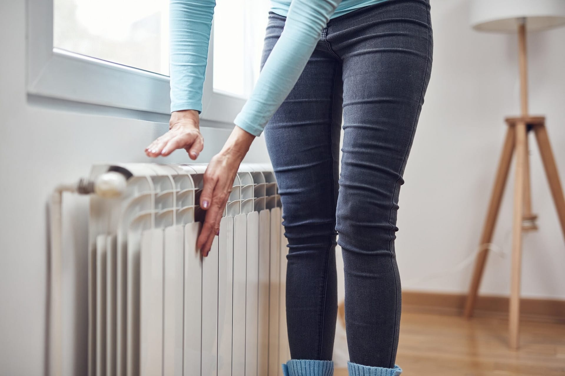 Woman heating her hands on the radiator during cold winter days.