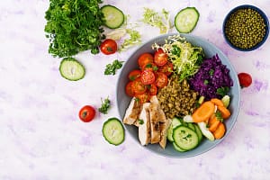 Healthy salad with chicken, tomatoes, cucumber, lettuce, carrot, celery, red cabbage and mung bean on light background. Proper nutrition. Dietary menu. Flat lay. Top view Healthy salad with chicken, tomatoes, cucumber, lettuce, carrot, celery, red cabbage and mung bean on light background.