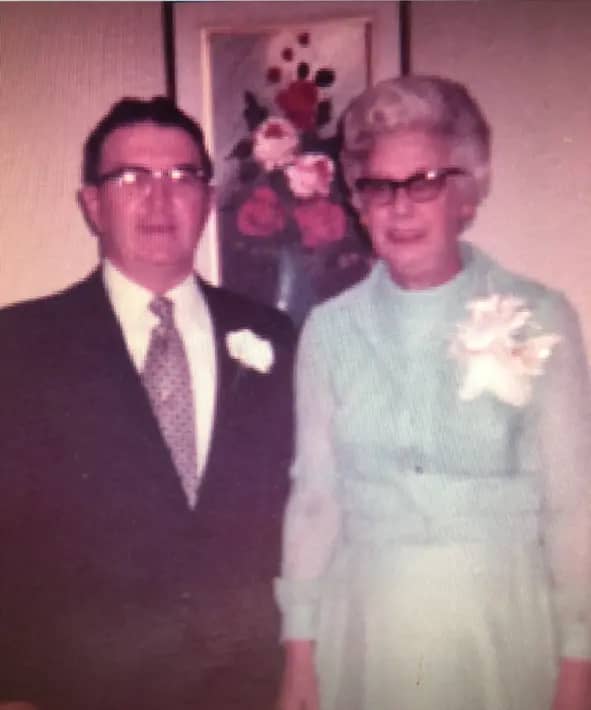 Clement Jr. and his wife wearing formal clothing in front of a floral artpiece