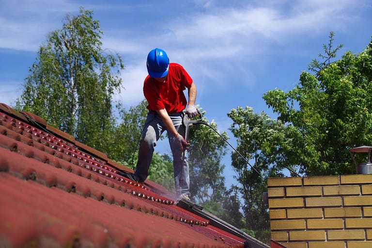 House roof cleaning with pressure tool. Worker on top of building washing tile with professional equipment. Moss removing with water.