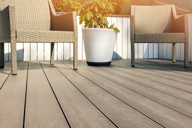 Two wicker chairs sit on a composite deck next to a large white planter with a green leafy plant