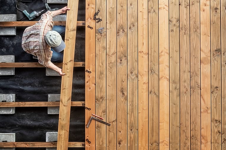 A person wearing a cap and plaid shirt installs wooden decking boards