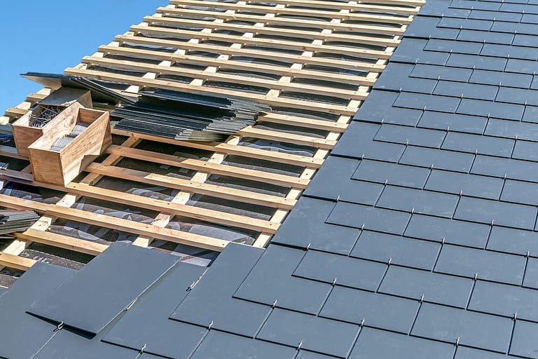 Partially completed roof showing wooden framework and stacks of composite slate tiles