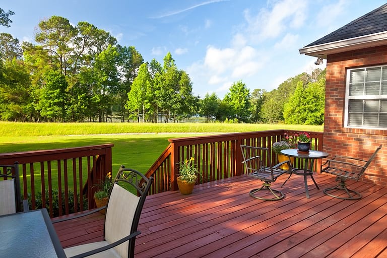 A raised deck with a glass table and chairs overlooks a green lawn and trees, highlighting the openness compared to ground level.