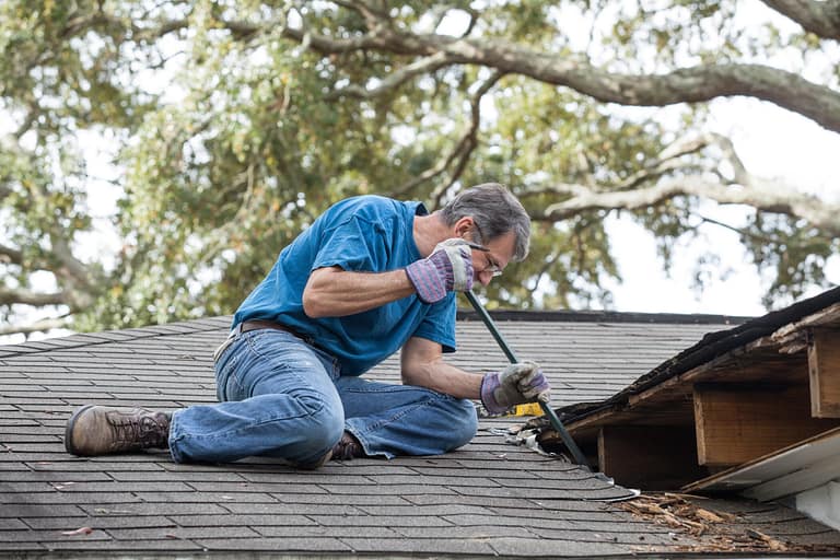 Homeowner on roof uses crowbar to remove damaged flashing and shingles on leaky roof