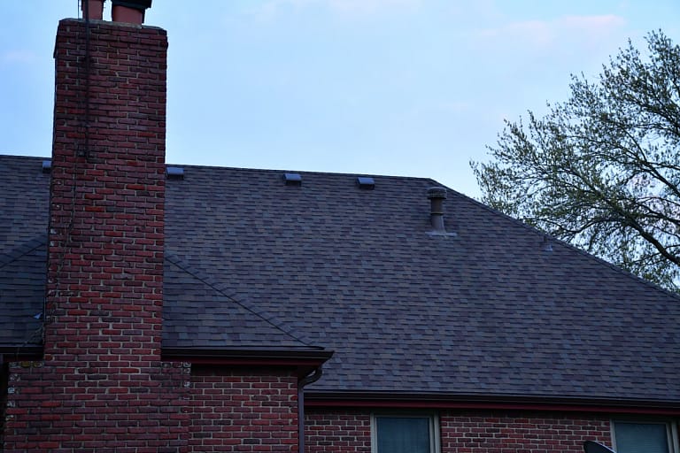 dark shingle and brick chimney home with roof vents scattered over rooftop