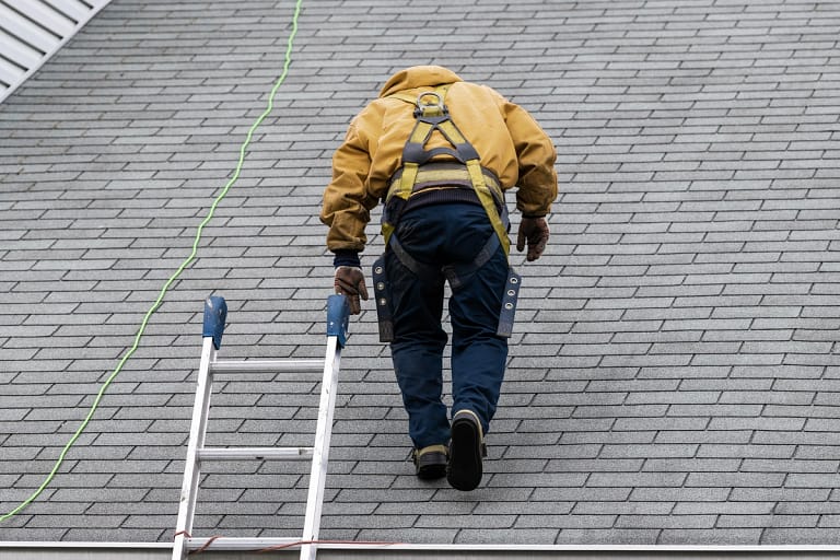 A roofer walks on an asphalt shingle roof
